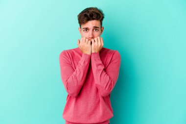 Mavi arka planda izole edilmiş, tırnak yiyen, gergin ve endişeli genç bir beyaz adam..