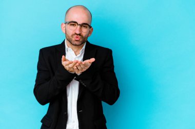 Genç, beyaz, kel bir adam mavi arka planda izole edilmiş dudaklar kıvrılmış ve hava öpücüğü vermek için avuç içleri tutulmuş..