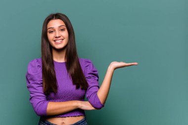 Mavi arka planda izole edilmiş genç Hintli kadın bir avuç içinde fotokopi alanı ve belinde bir el daha olduğunu gösteriyor..