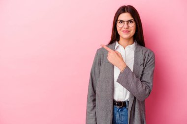 Genç beyaz iş kadını pembe arka planda izole edilmiş gülümsüyor ve boş alanda bir şeyler gösteriyor..