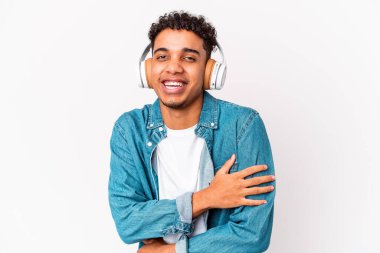Genç Afro-Amerikalı kıvırcık adam, izole edilmiş kulaklıklı müzik dinliyor kahkahalar atıyor, elini göğsünde tutuyor..