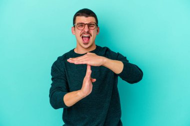 Mavi arka planda izole edilmiş genç beyaz bir adam bir mola hareketi gösteriyor..