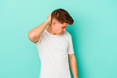 Kafkasyalı genç adam mavi arka planda izole edilmiş. Stres yüzünden boynu ağrıyor. Masaj yapıyor ve elle dokunuyor..