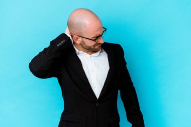 Genç, beyaz, kel bir adam mavi arka planda izole edilmiş. Stres yüzünden boynu ağrıyor, masaj yapıyor ve elle dokunuyor..