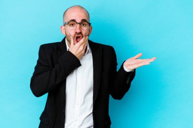 Mavi arka planda izole edilmiş beyaz saçlı genç bir adam bir avuç içinde fotokopi alanı tutuyor, el üstünde tutuyor. Şaşırmış ve mutlu..