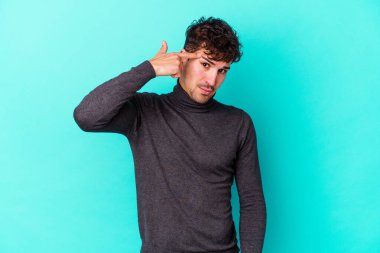 Mavi arka planda izole edilmiş genç beyaz adam işaret parmağıyla bir hayal kırıklığı jesti gösteriyor..