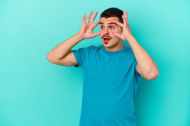 Mavi arka planda izole edilmiş genç beyaz adam bir başarı fırsatı bulmak için gözlerini açık tutuyor..