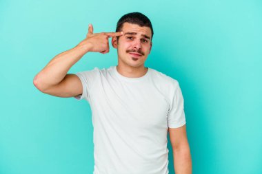 Mavi arka planda izole edilmiş genç beyaz adam işaret parmağıyla bir hayal kırıklığı jesti gösteriyor..