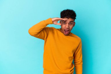 Genç Afro-Amerikalı kıvırcık adam mavi üzerine izole edilmiş yüksek sesle bağırıyor, gözlerini açık ve ellerini gergin tutuyor..