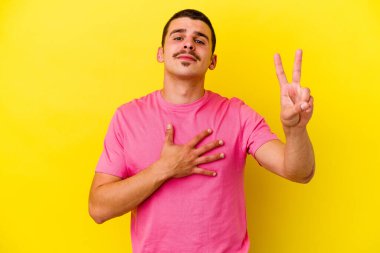 Beyaz tenli genç adam sarı arka planda izole edilmiş yemin ediyor, elini göğsüne koyuyor..