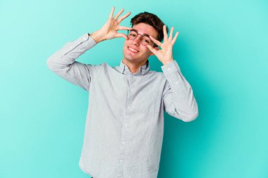 Mavi arka planda izole edilmiş genç beyaz adam gözlerinde sorun olmadığını gösteriyor.