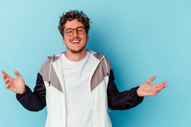 Gözlük takan genç beyaz adam mavi arka planda izole edilmiş neşeli bir şekilde gülüyor. Mutluluk kavramı.