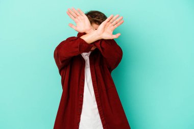 Kafkasyalı genç adam mavi arka planda izole edilmiş iki kolu çapraz tutuyor, inkar kavramı.