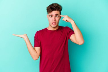 Kafkasyalı genç adam mavi arka planda izole edilmiş ve elinde bir ürün tutuyor..