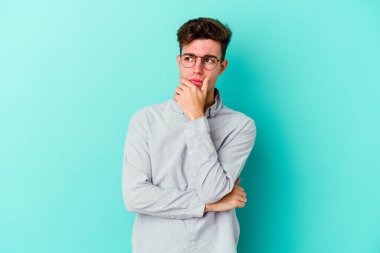 Kafkasyalı genç adam mavi arka planda izole edilmiş şüpheli, belirsiz, seni muayene ediyor..