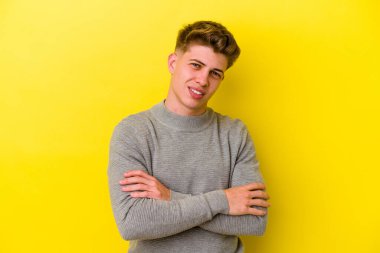 Sarı arka planda izole edilmiş genç beyaz adam kendini güvende hissediyor, kararlılıkla kollarını kavuşturuyor..