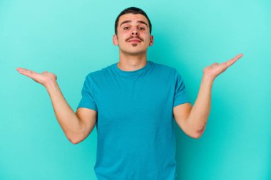 Kafkasyalı genç adam mavi arka planda izole edilmiş. Kafası karışmış ve omuz silkiyor. Kopya alanını tutmak için..