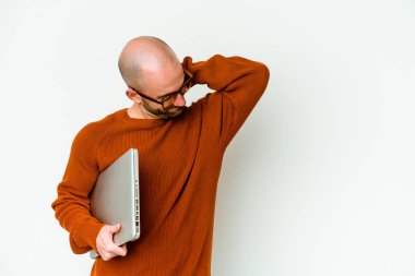 Genç ve kel bir adam dizüstü bilgisayarını beyaz arka planda saklayıp kafasının arkasına dokunuyor, düşünüyor ve bir seçim yapıyor..