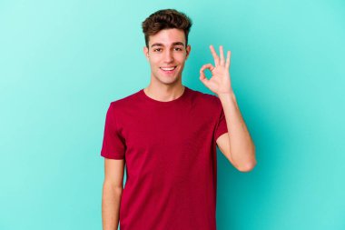Kafkasyalı genç adam mavi arka planda izole edilmiş neşeli ve kendinden emin..
