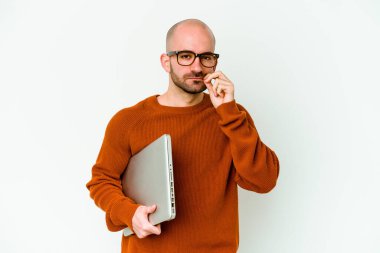 Diz üstü bilgisayarı olan genç kel bir adam beyaz arka planda izole edilmiş ve parmakları dudaklarında bir sır saklıyor..