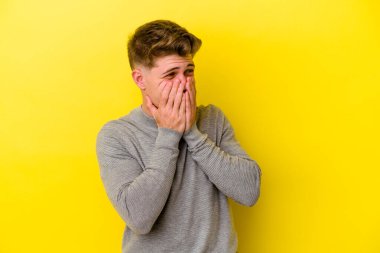 Sarı arka planda izole edilmiş genç beyaz bir adam bir şeye gülüyor, ağızlarını ellerle kapatıyor..