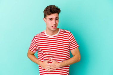 Mavi arka planda karaciğer ağrısı çeken, karnı ağrıyan genç beyaz bir adam..