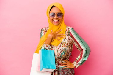 Genç müslüman kadın pembe arka planda izole giysiler alıyor..