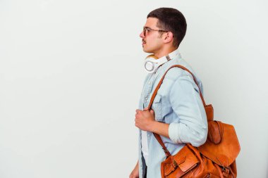 Beyaz arka planda müzik dinleyen beyaz tenli genç bir öğrenci sola bakıyor, yan pozlar veriyor..