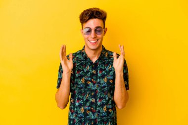 Hawaii gömleği giyen genç beyaz bir adam sarı arka planda izole edilmiş neşeli bir şekilde gülüyor. Mutluluk kavramı.