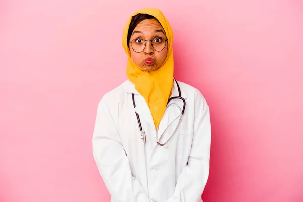 Young doctor muslim woman isolated on pink background blows cheeks, has tired expression. Facial expression concept.