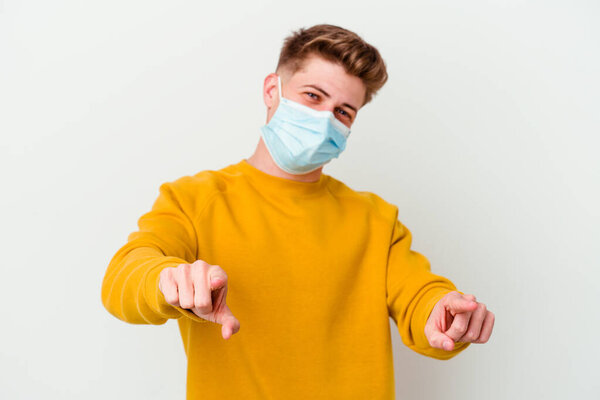 Young man wearing a mask for coronavirus isolated on white background cheerful smiles pointing to front.