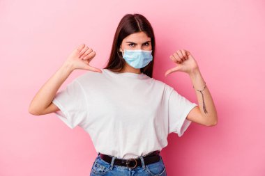 Pembe arka planda izole edilmiş virüs maskesi takan beyaz bir kadın gururlu ve kendinden emin hissediyor..
