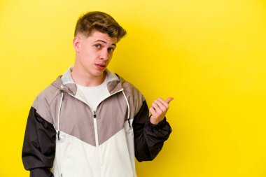 Kafkasyalı genç adam sarı arka planda izole edilmiş, başparmak uzakta, gülüyor ve kaygısız..