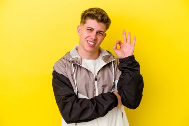 Sarı arka planda izole edilmiş genç beyaz bir adam bir göz kırptı ve elleriyle iyi bir jest yaptı..