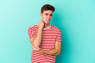 Kafkasyalı genç adam mavi arka planda izole edilmiş dirsek masajı yapıyor, kötü bir hareketin ardından acı çekiyor..