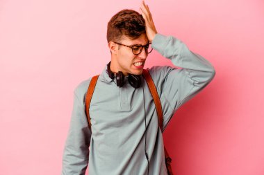 Pembe arka planda izole olmuş genç bir öğrenci bir şeyi unutuyor. Alnına avuç içi ve kapalı gözlerle vuruyor..