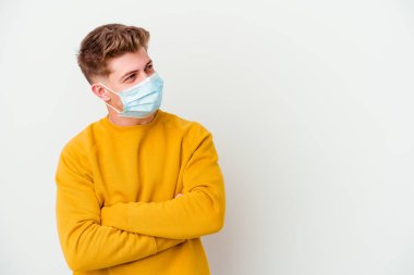 Koronavirüs maskesi takan genç adam beyaz arka planda izole edilmiş, kollarını kavuşturarak gülümsüyor..