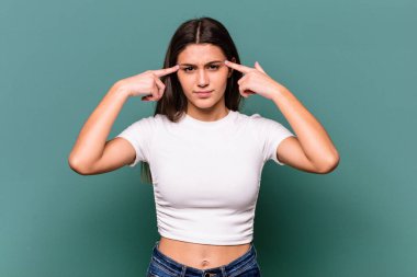 Mavi arka planda izole edilmiş genç Hintli kadın bir göreve odaklanmış, işaret parmaklarını işaret ediyor..