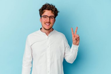 Kafkasyalı genç iş adamı mavi arka planda izole edilmiş zafer işareti gösteriyor ve gülümsüyor..