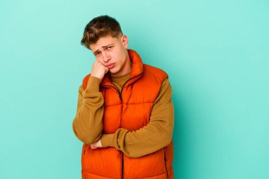 Mavi arka planda izole edilmiş genç beyaz adam tekrarlanan bir görevden yoruldu..