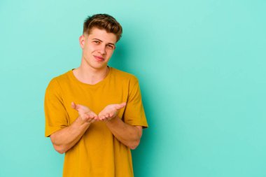 Kafkasyalı genç adam mavi arka planda izole edilmiş dudaklar kıvrılıyor ve hava öpücüğü göndermek için avuç içleri tutuyor..