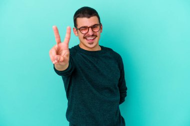 Mavi arka planda izole edilmiş genç beyaz adam iki numarayı parmaklarıyla gösteriyor..