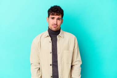 Kafkasyalı genç adam mavi arka planda izole edilmiş üzgün, ciddi yüzlü, mutsuz ve hoşnutsuz..