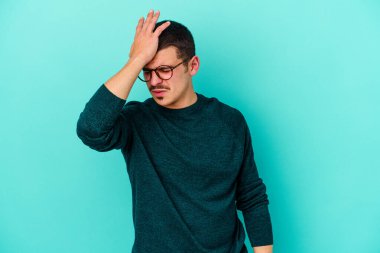 Kafkasyalı genç adam mavi arka planda izole edilmiş bir şekilde bir şeyi unutuyor. Alnına avuç içi ve gözlerini kapayarak vuruyor..