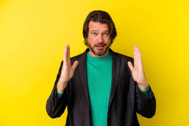 Orta yaşlı beyaz bir adam sarı arka planda izole edilmiş. Elinde işaret parmaklarıyla küçük bir şey tutuyor, gülümsüyor ve kendinden emin..