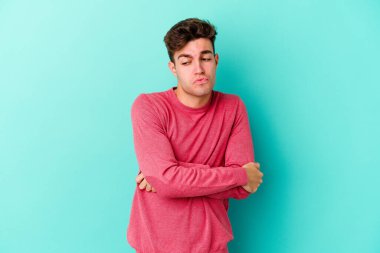 Mavi arka planda izole edilmiş genç beyaz adam tekrarlanan bir görevden yoruldu..