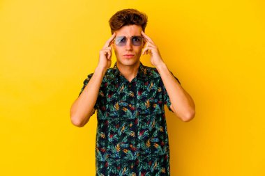 Hawaii gömleği giyen genç beyaz adam sarı arka planda izole edilmiş vazifesine odaklanmış, parmak uçlarını işaret ediyor..