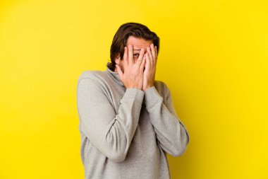 Orta yaşlı, beyaz bir adam sarı arka planda izole edilmiş. Korkmuş ve gergin parmaklarıyla göz kırp..