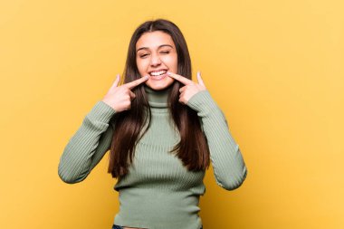 Sarı arka planda izole edilmiş genç Hintli kadın gülümsüyor, parmaklarını ağzına doğrultuyor..