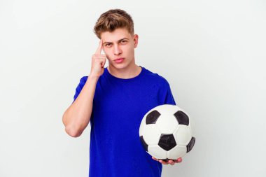 Arka planda izole bir şekilde futbol oynayan beyaz bir adam şakağı parmağıyla işaret ediyor, düşünüyor ve bir göreve odaklanıyor..